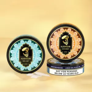Alibarbar Nicotine Pouches - Two Decorative Nicotine Pouch Tins with Turquoise and Orange Mandala Labels Resting on a Beige Surface; Warning Can Reads 'not for Persons Below 18 Years Old' on the Bottom Can. - Iget Vapes Shop Oz