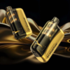 Two gold and black vape devices suspended against a glossy metallic gold background, showcasing their tanks and rounded shapes.